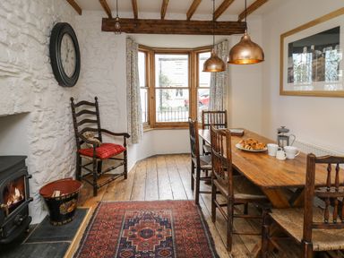 A dining room with a wooden table and chairs a bay window and a fireplace at Ty Len in St Davids