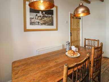 A wooden dining table with pastries cups and a coffee press with wooden chairs in a dining room at Ty Len in St Davids