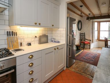 A kitchen with white cabinets knives on a wooden block and a stainless steel refrigerator next to a dining area with a wooden chair and a patterned rug at Ty Len in St Davids
