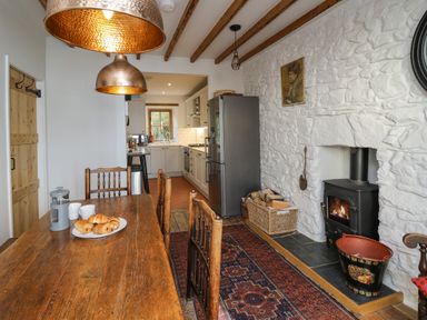 A kitchen and dining area with wooden table and chairs wood burning stove and stainless steel refrigerator at Ty Len in St Davids