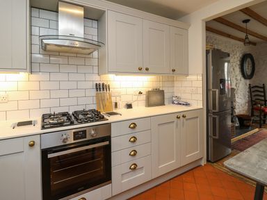 A kitchen with white cabinets a gas stove an oven a stainless steel fridge and white tiled walls at Ty Len in St Davids