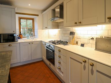 A kitchen with white cabinets a gas stove an oven a microwave and a window at Ty Len in St Davids