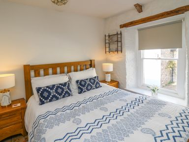 A bedroom with a wooden bed framed with blue patterned bedding two bedside tables with lamps and a window with a beige blind and flowers on the sill at Ty Len in St Davids