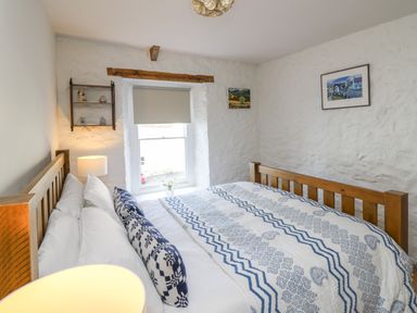 A bedroom with a wooden bed with patterned bedding a window with a blind a lamp and framed pictures on white textured walls at Ty Len in St Davids
