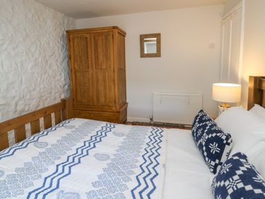 A bedroom with a wooden bed with white and blue bedding a wooden wardrobe a small mirror and a lamp at Ty Len in St Davids