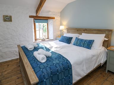 A bedroom with a wooden bed and blue bedding next to a window with a wooden frame at Ty Len in St Davids