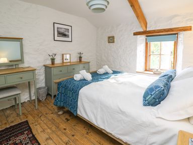 A bedroom with a bed covered in white and blue linens beside a wooden dresser and vanity at Ty Len in St Davids