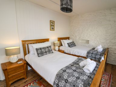 A bedroom with two wooden beds with white bedding and gray patterned throws at Ty Len in St Davids