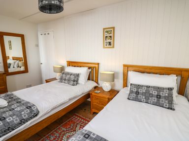 A bedroom with two single beds with wooden headboards bedside tables and lamps at Ty Len in St Davids