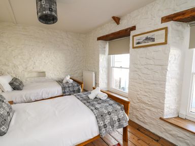 A bedroom with two single beds wooden floors and white stone walls at Ty Len in St Davids