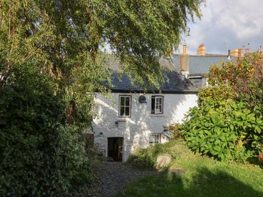 A white stone house with a slate roof partially hidden by trees and bushes at Ty Len in St Davids