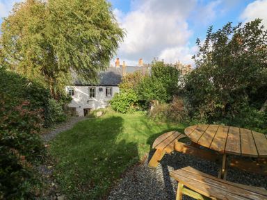 A garden with a wooden picnic table and benches surrounded by trees and bushes at Ty Len in St Davids