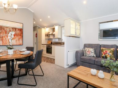 An open plan living room and kitchen with a dining table set and a grey sofa with cushions at Squirrels Nook Waterside Wood 19 White Cross Bay near Windermere