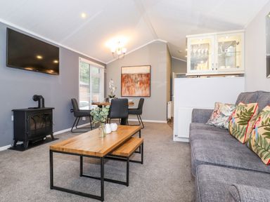 A living room with a grey sofa with patterned cushions a wooden coffee table and a dining table with four chairs at Squirrels Nook in Waterside Wood 19 White Cross Bay near Windermere