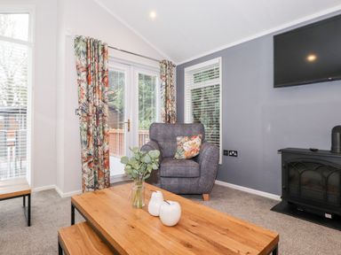 A living room with a gray armchair and floral cushions near windows and a wood coffee table with decorative items at Squirrels Nook in Waterside Wood 19 White Cross Bay near Windermere