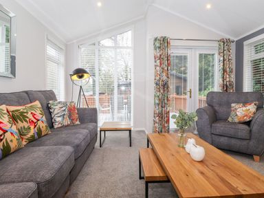 A living room with grey sofas a wooden coffee table and floral cushions at Squirrels Nook in Waterside Wood 19 White Cross Bay near Windermere