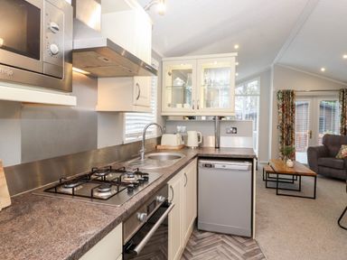 A kitchen with countertop stove microwave sink dishwasher and kettle opening into a living room at Squirrels Nook Waterside Wood 19 White Cross Bay near Windermere