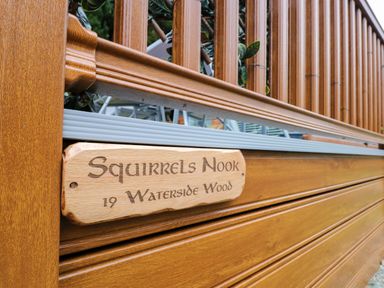 A wooden fence with a carved wooden sign that reads Squirrels Nook 19 Waterside Wood