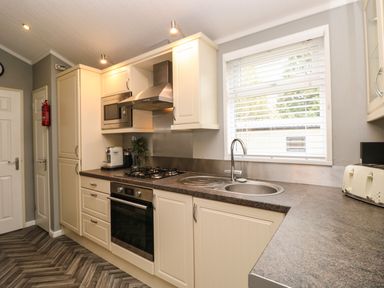 A kitchen with cream cabinets a gas stove microwave sink and window at Squirrels Nook in Waterside Wood 19 White Cross Bay near Windermere