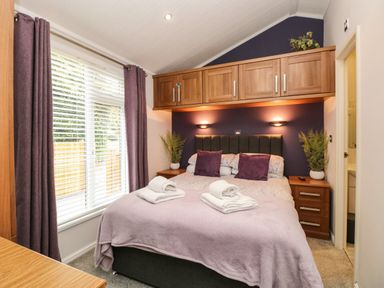 A bedroom with a bed with folded towels bedside tables with plants and built in cupboards above the bed at Squirrels Nook in Waterside Wood 19 White Cross Bay near Windermere