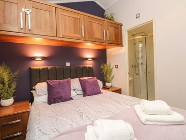 A bedroom with a double bed purple pillows wooden cabinets and an ensuite shower at Squirrels Nook in Waterside Wood 19 White Cross Bay near Windermere