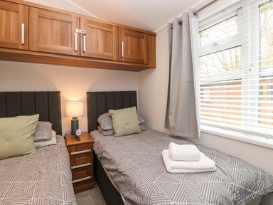A bedroom with two single beds a bedside table lamp and a window with curtains at Squirrels Nook Waterside Wood 19 White Cross Bay near Windermere