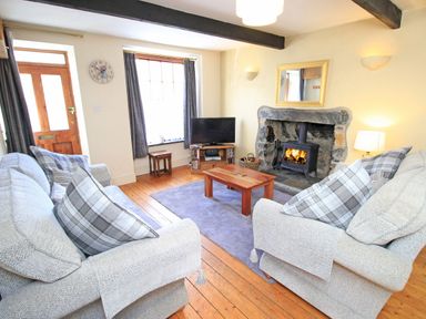 A living room with two sofas a wooden coffee table a rug a television a fireplace and wooden flooring at Hafan Cottage in Beddgelert