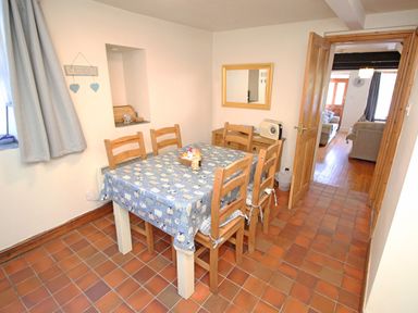A dining room with a table covered by a blue tablecloth and six wooden chairs at Hafan Cottage in Beddgelert