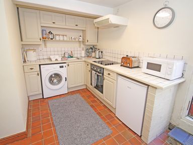 A kitchen with white cabinets washing machine oven small refrigerator microwave and toaster at Hafan Cottage in Beddgelert