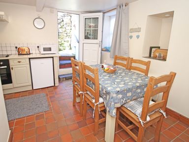 A kitchen with a wooden dining table covered with a patterned tablecloth and six chairs next to a door leading outside at Hafan Cottage in Beddgelert