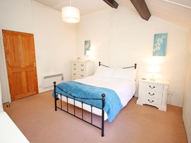 A bedroom with a double bed a blue throw two white bedside tables with lamps and a wooden door at Hafan Cottage in Beddgelert
