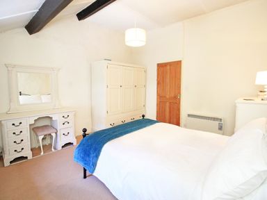 A bedroom with a bed a white dresser a white wardrobe and a wooden door at Hafan Cottage in Beddgelert