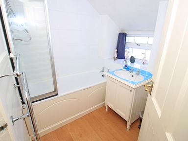 A bathroom with a bathtub shower combination a sink with a blue tiled countertop a window with blue curtains and decorative duck figurines at Hafan Cottage in Beddgelert