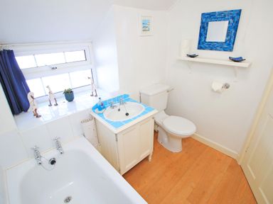 A bathroom with a bathtub sink and toilet wooden floor and blue framed mirror at Hafan Cottage in Beddgelert