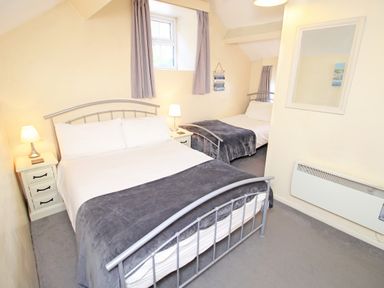 A bedroom with two beds bedside lamps a wall mirror and a window at Hafan Cottage in Beddgelert