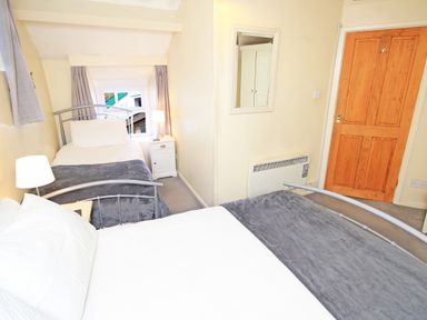 A bedroom with two beds a nightstand with a lamp a mirror on the wall and a wooden door at Hafan Cottage in Beddgelert