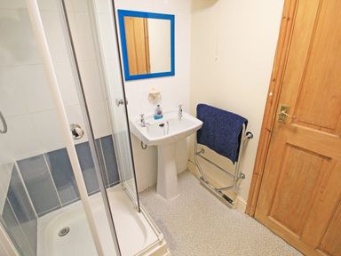 A bathroom with a shower enclosure pedestal sink mirror and towel rail at Hafan Cottage in Beddgelert