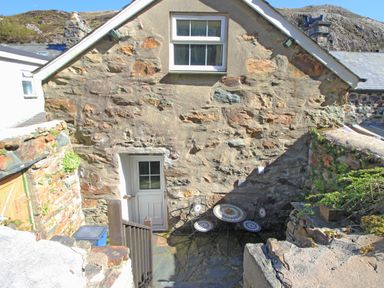 A stone cottage with a small outdoor seating area and stairs leading down to a white door at Hafan Cottage in Beddgelert