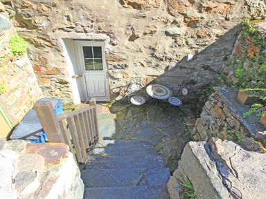 Stone steps leading down to a small patio area with a white door two blue bins and a round table with two chairs at Hafan Cottage in Beddgelert