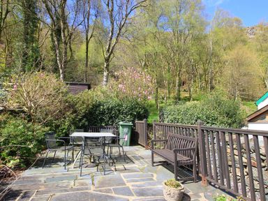 An outdoor patio with metal chairs and table wooden benches and plants at Hafan Cottage in Beddgelert