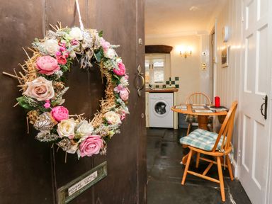 A floral wreath on a door with a small dining table and chairs in a kitchen at Gardeners Cottage in Millom Cumbria