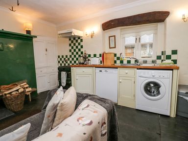 A kitchen area with a washing machine dishwasher countertop and wood stack at Gardeners Cottage Millom Cumbria