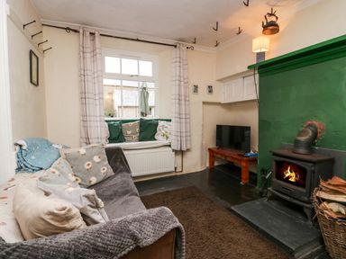 A living room with a wood burning stove sofa cushions window seat and television at Gardeners Cottage in Millom Cumbria