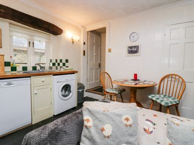 A kitchen area with a washing machine dishwasher sink and a small dining table with two chairs at Gardeners Cottage in Millom Cumbria