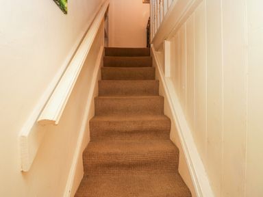 A carpeted staircase with beige walls and a wooden handrail at Gardeners Cottage in Millom Cumbria