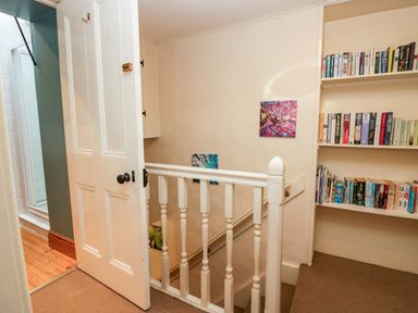 A staircase landing with a white railing and built in bookshelves filled with books at Gardeners Cottage in Millom Cumbria