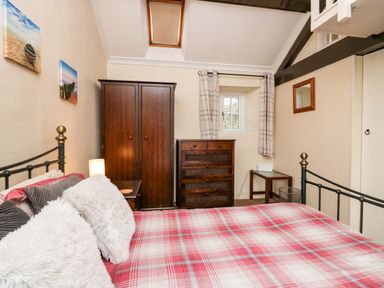 A bedroom with a bed covered in a red plaid blanket wooden wardrobe chest of drawers and a small window at Gardeners Cottage Millom Cumbria