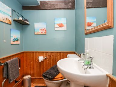 A bathroom with a sink mirror toilet towels and beach-themed pictures at Gardeners Cottage Millom Cumbria