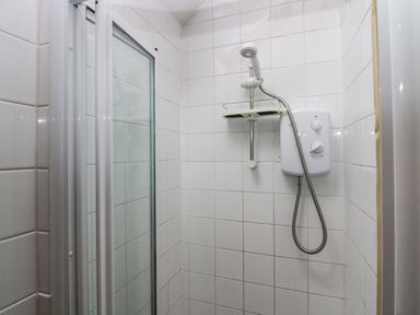 A shower cubicle with white tiled walls a showerhead and a control unit at Gardeners Cottage in Millom Cumbria
