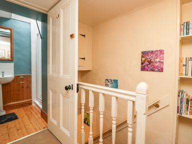A staircase with white wooden railing leading to a landing with an open door to a bathroom and a bookshelf with books at Gardeners Cottage Millom Cumbria
